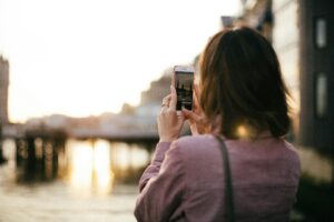 A photo of a woman taking a photo with her phone of a bridge in London, England. This is to illustrate the points in the article called 3 tips for making the most of an overseas conference as a freelancer