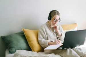 Stock image of a young woman sitting on a couch wearing headphones and looking at her laptop. This is to illustrate the article on New Year's resolutions for freelancers 